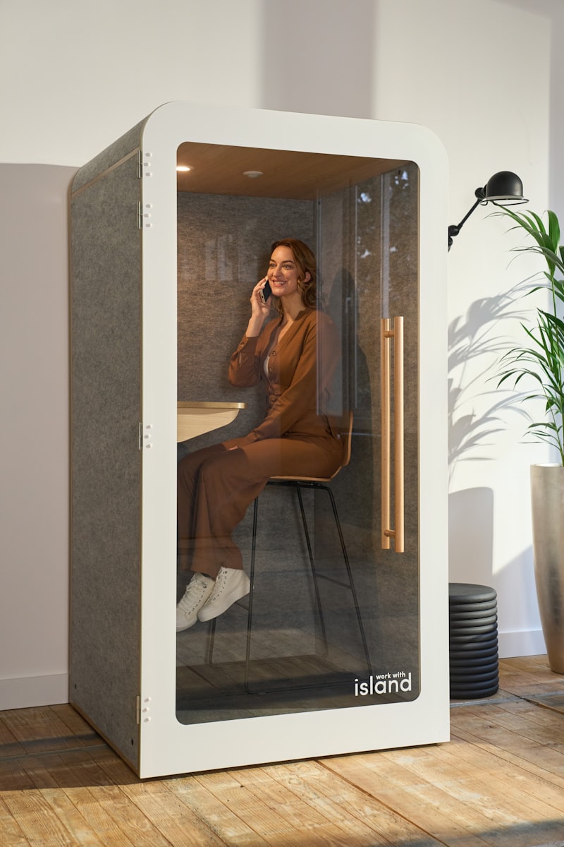 A person taking a private phone call while seated inside a single-person acoustic phone booth