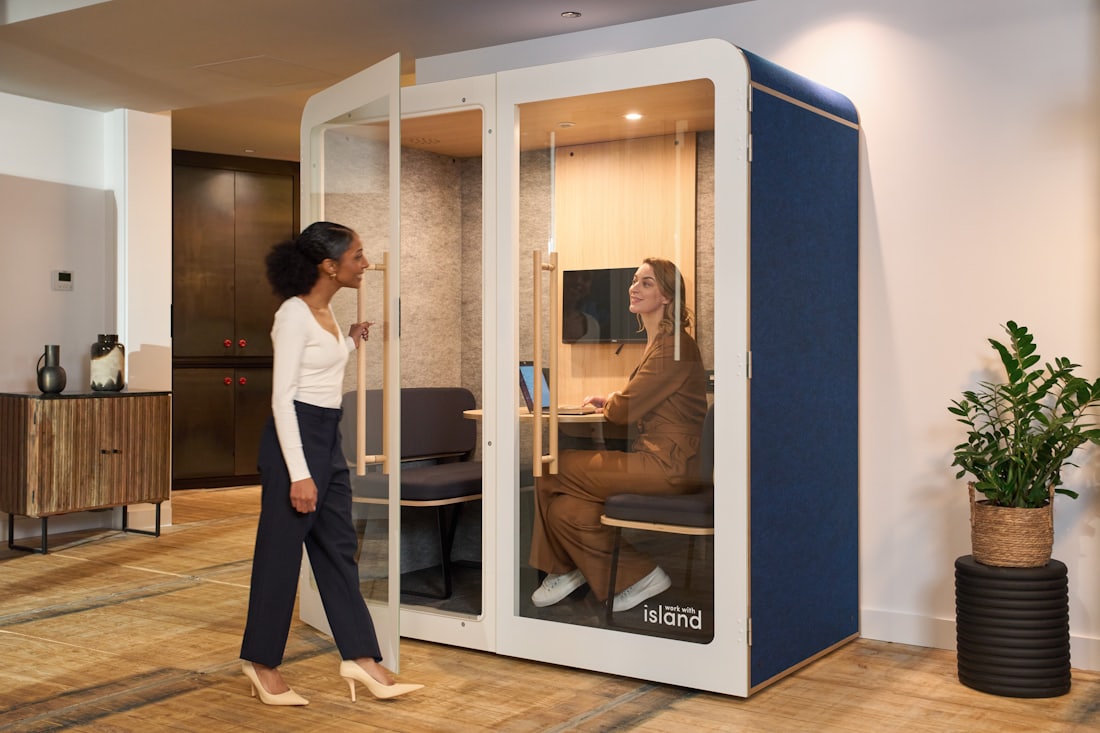 An acoustic office pod installed on an open-plan floor, with a colleague walking towards its door